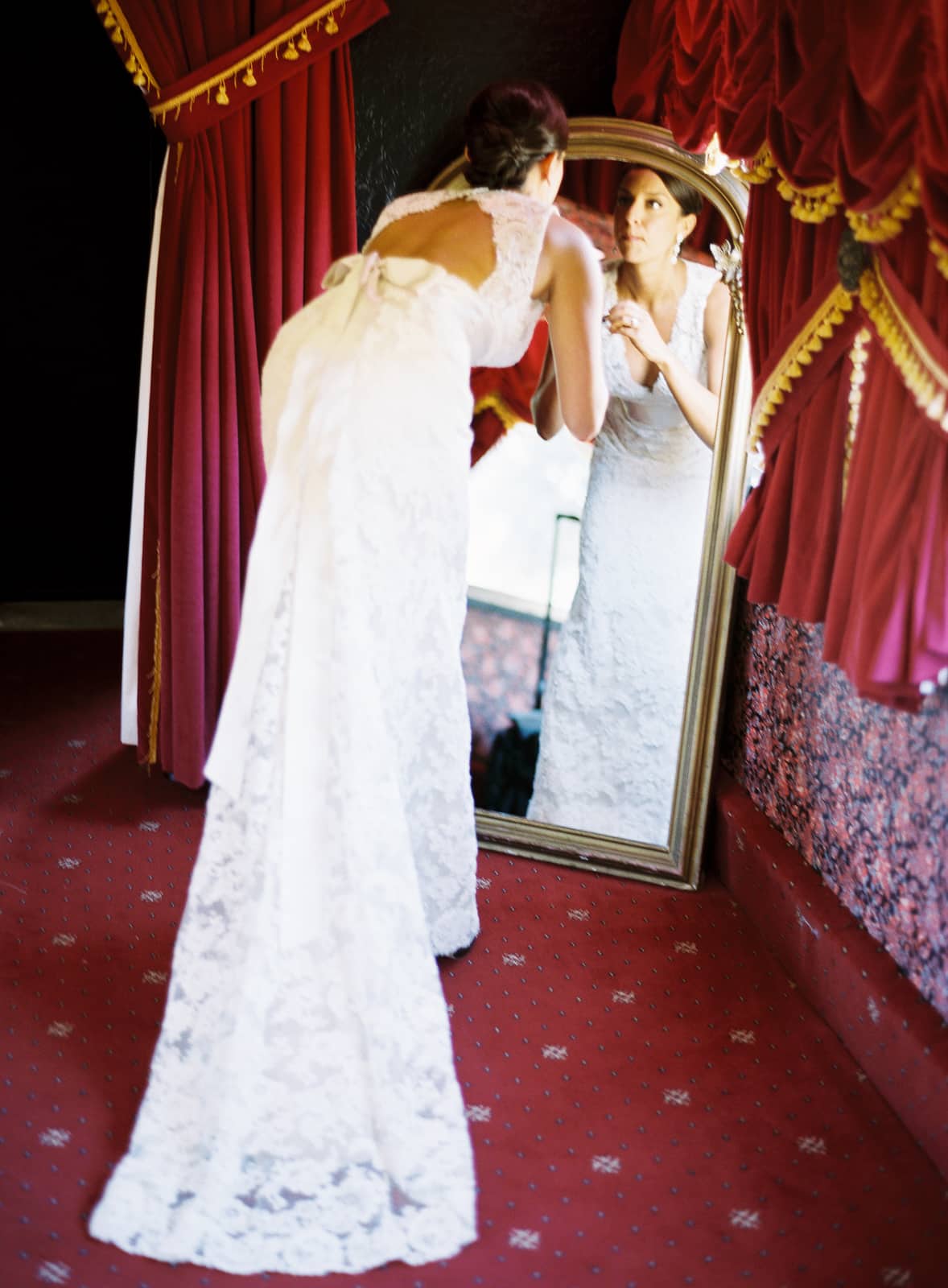 Bride checking her makeup in the mirror with red drapes