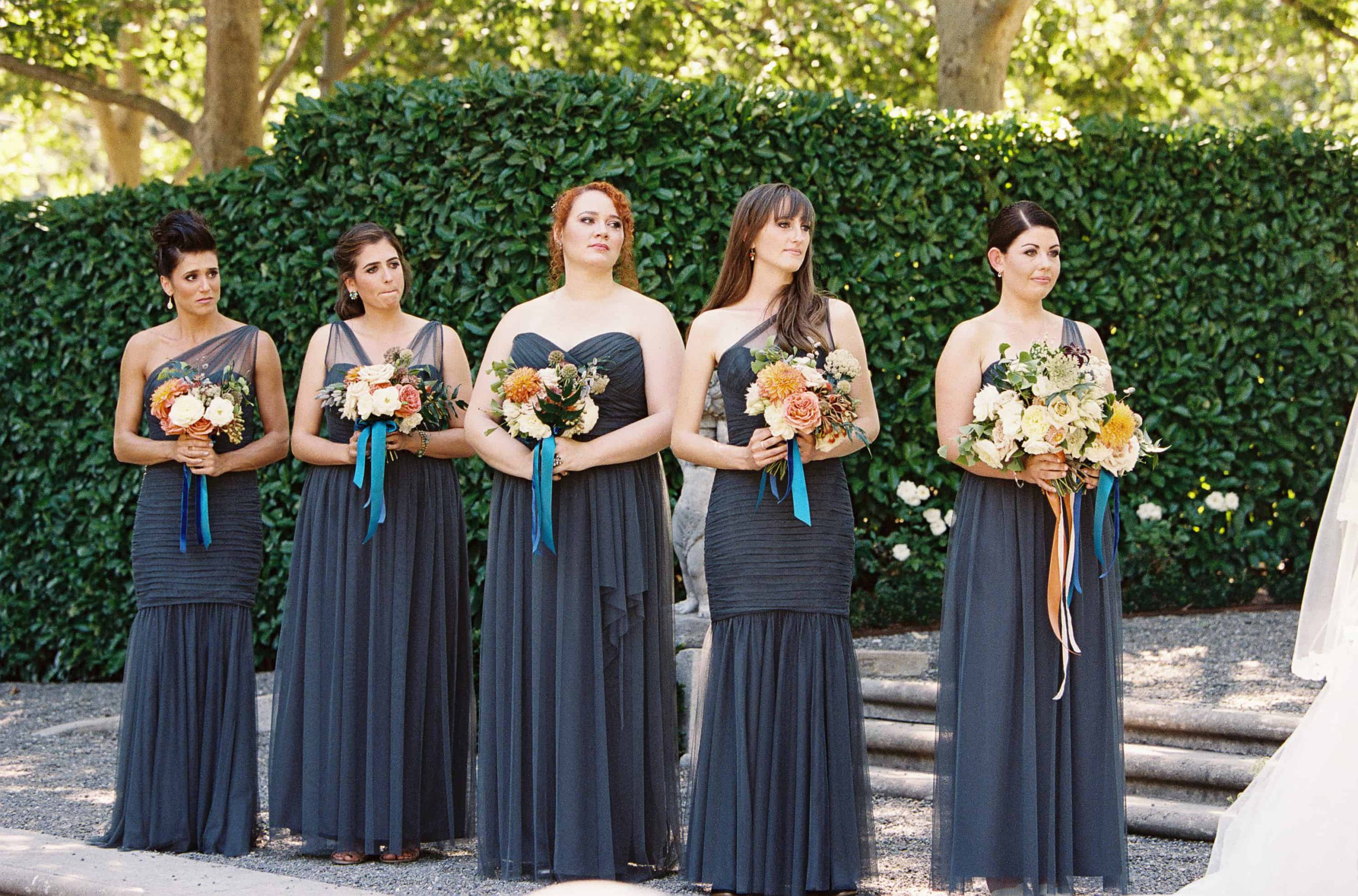 bridesmaids in gray dresses holding orange and white bouquets