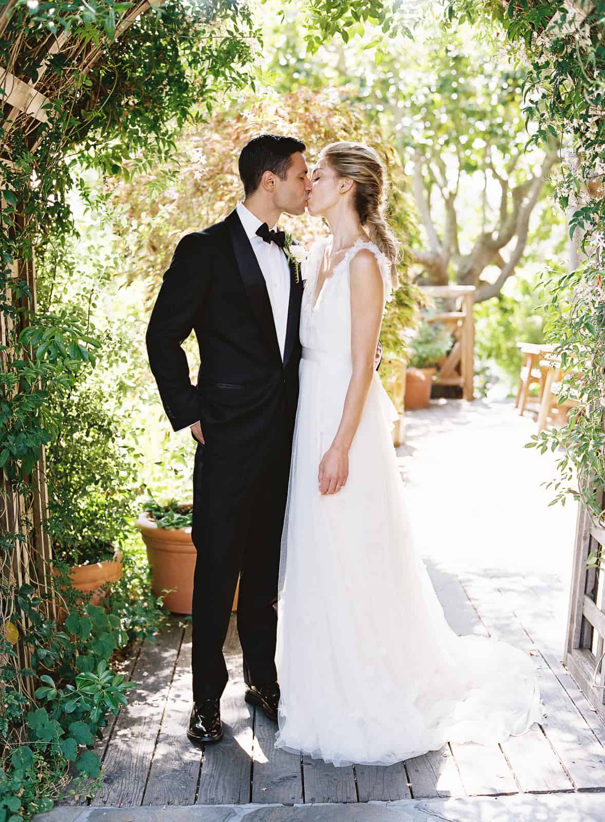 bride and groom kiss under trellis