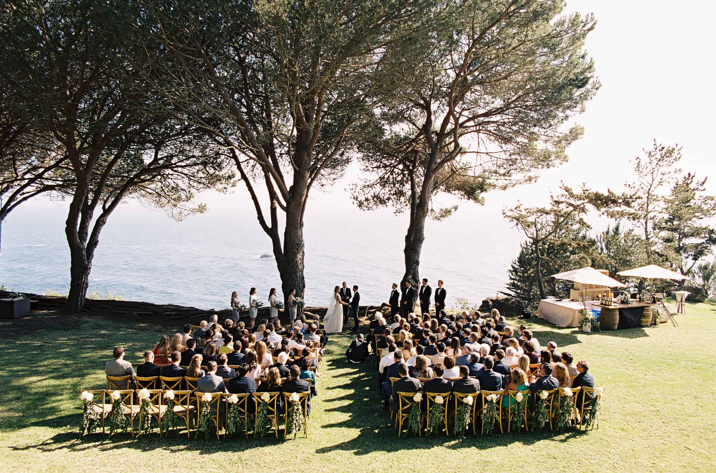 outdoor seaside ceremony with ocean trees and grass lawn