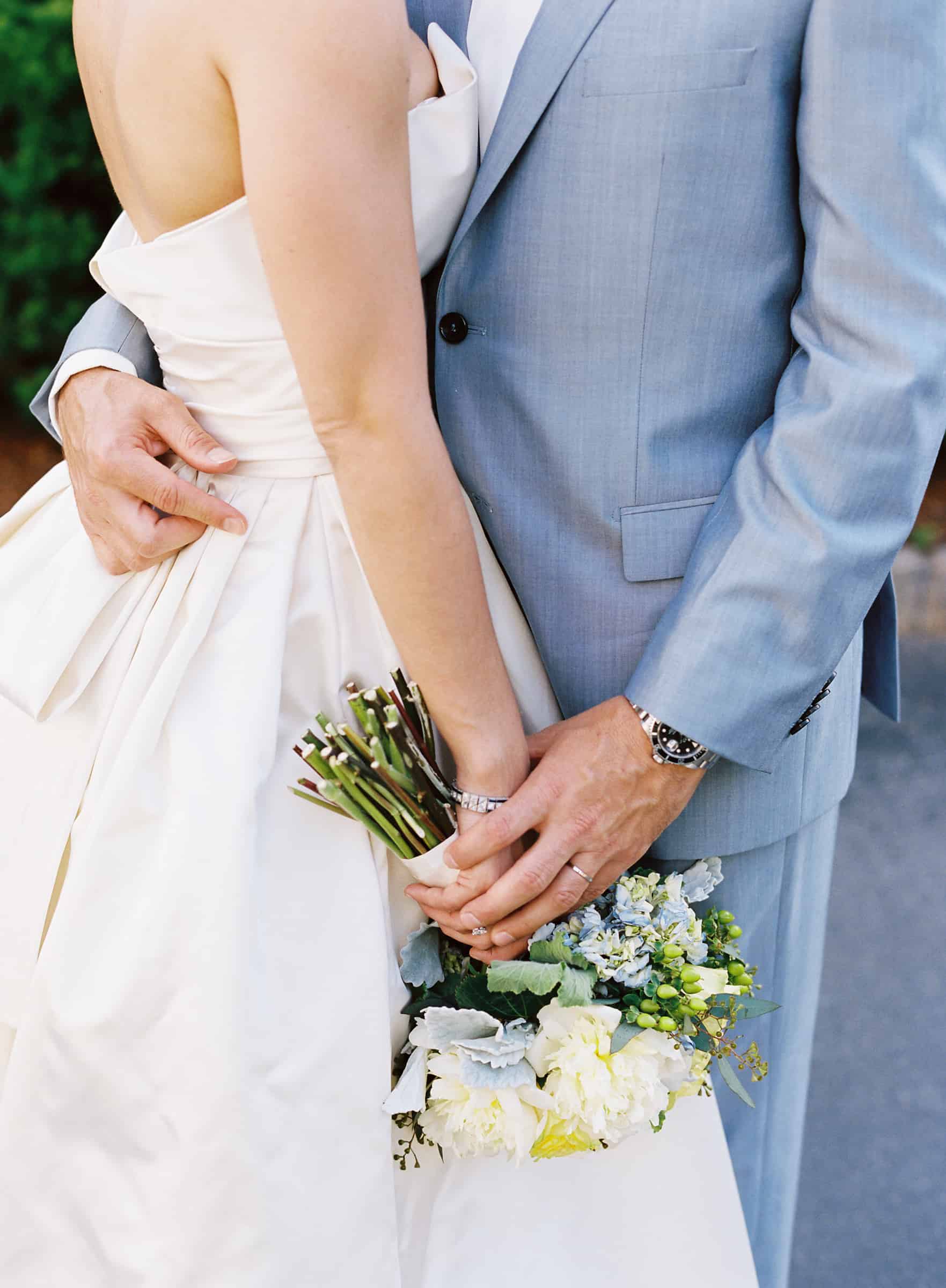 closeup of a bride in an Amsale dress and a groom in a baby blue suit holding hands